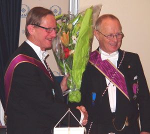 Den avtroppende Ordf.br. Rolf Schjem (t.h.) og påtroppende Jan Holt er venner og kamerater gjennom mange år, både i loge og på arbeidssted. Her utveksler de blomster, takk og lykkeønskninger.