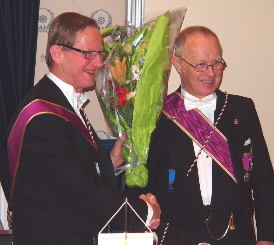 Den avtroppende Ordf.br. Rolf Schjem (t.h.) og påtroppende Jan Holt er venner og kamerater gjennom mange år, både i loge og på arbeidssted. Her utveksler de blomster, takk og lykkeønskninger.